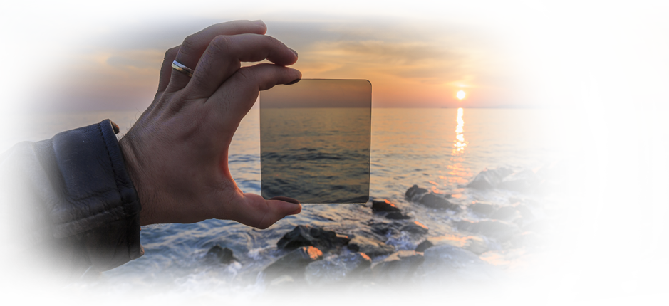 Hand holding filter against sunrise over rocky coast | American Polarizers, Inc.